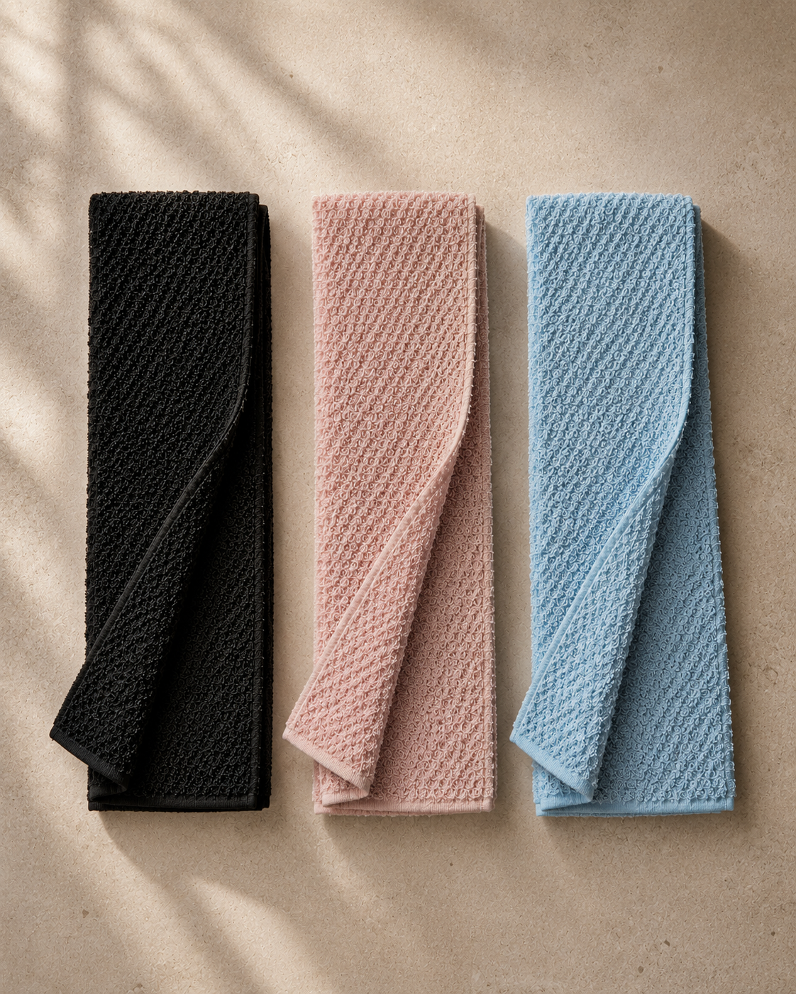 Black pink and blue Kuyona exfoliating towels arranged on warm stone
